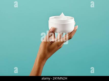 Cachez votre main de lotion pour le corps noire féminine dans un pot blanc vierge sur fond turquoise Banque D'Images