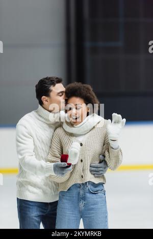 Une femme afro-américaine excitée qui regarde la proposition sonne en main avec un petit ami sur la patinoire Banque D'Images
