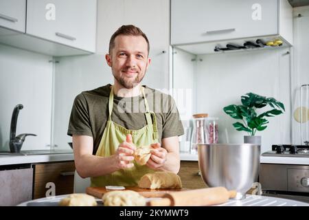 Boulanger de chef caucasien gai en tablier vert faisant des boules de pâte avec planche à découper en bois sur fond. Cuisine maison, cuisine maison. Photo de haute qualité Banque D'Images