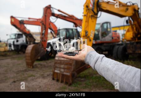 la main de l'homme tient une petite pelle dans sa paume. Derrière lui, hors de vue, une rangée de pelles hydrauliques réelles avec de grands godets. Exploitation des pelles hydrauliques. A Banque D'Images