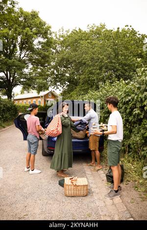 La famille s'aidant les uns les autres tout en chargeant les fournitures de pique-nique dans le coffre de voiture Banque D'Images