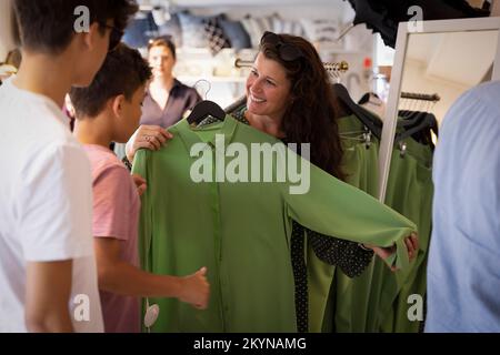 Bonne femme montrant une robe verte à des fils debout en magasin Banque D'Images