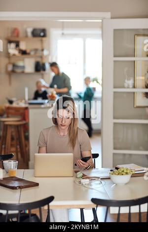 Femme d'affaires tenant un smartphone tout en travaillant sur un ordinateur portable à la maison Banque D'Images
