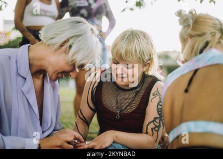 Sourire personne non binaire appliquant vernis à ongles à l'ami assis par la femme Banque D'Images