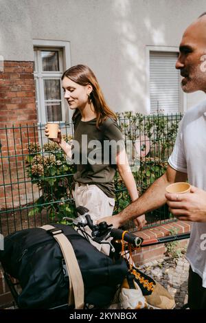 Jeune femme avec un ami de sexe masculin en train de rouler à vélo tout en prenant un café Banque D'Images