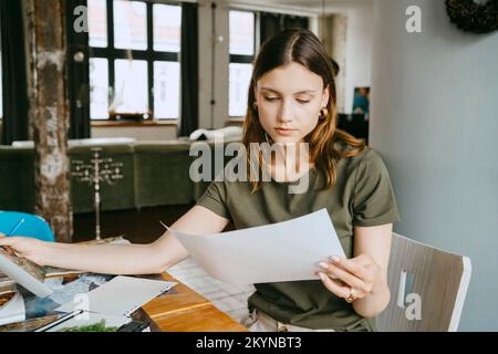 La styliste féminine concentrée de l'alimentation tient une photo tout en travaillant en studio Banque D'Images