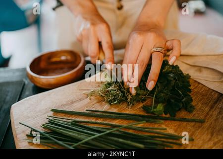 Les mains du chef féminin hacher des légumes à feuilles sur une planche à découper en studio Banque D'Images