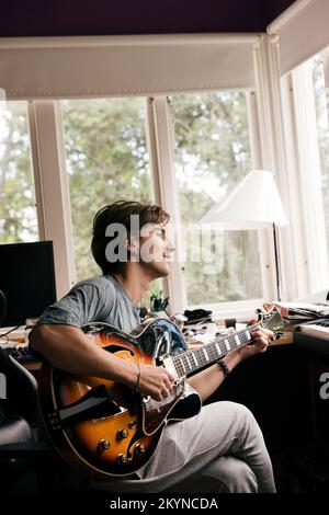 Vue latérale de l'homme pratiquant la guitare tout en étant assis à la maison Banque D'Images