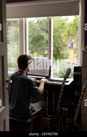 Vue arrière de l'homme lisant une note de musique tout en pratiquant le piano à la maison Banque D'Images