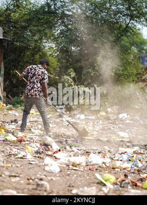 Homme balayant les ordures avec un balai et de la grande zone de déchets en polyhthène, homme nettoyant la zone polluée, journée de contrôle de la pollution, concept de pollution Banque D'Images