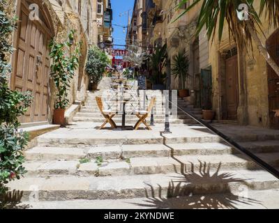 Valletta, Malte - Mai 2021: Tables de restaurant en bois sur les marches d'une rue étroite à la Valette, Malte. Banque D'Images