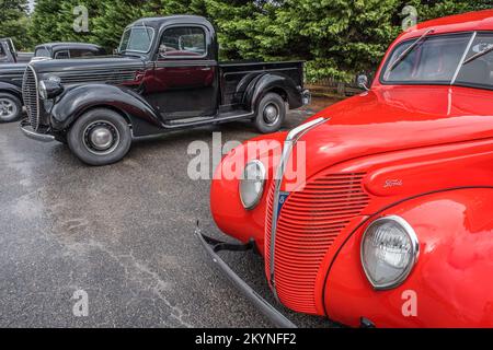 Vue partielle d'une vieille voiture de Ford restaurée rouge foncé garée par un camion noir des années 1930 à l'extérieur sous la pluie Banque D'Images