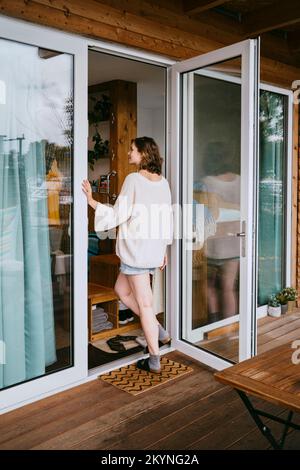 Vue arrière de la jeune femme entrant dans une petite maison Banque D'Images