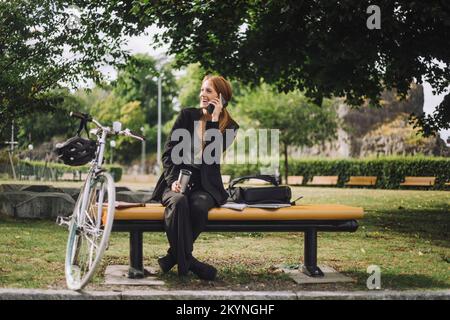Bonne femme d'affaires parlant sur un téléphone portable tout en étant assise à vélo au parc Banque D'Images
