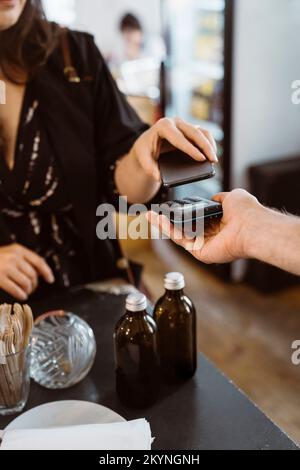 Section intermédiaire de la cliente de sexe féminin qui paie par simple pression et par téléphone intelligent au café Banque D'Images