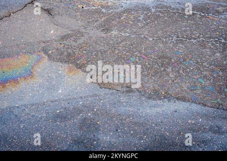 Fuite d'huile ou d'essence d'une voiture sur une route asphaltée mouillée et fissurée. Banque D'Images