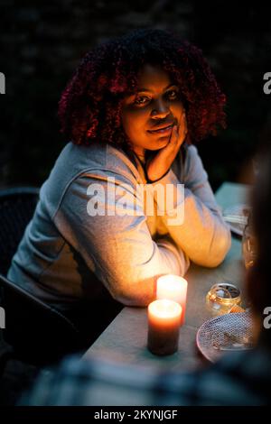 Portrait d'une jeune femme aux cheveux bouclés par une bougie illuminée sur une table à manger Banque D'Images