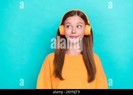 Photo de jeune positif mignon sourire adolescente écouter de la musique sans fil écouteurs à la recherche de rabais espace vide isolé sur fond de couleur cyan Banque D'Images