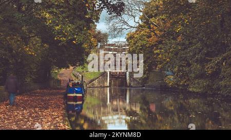 Péniche sur une voie navigable rurale ensoleillée, personne marchant sur le sentier, couleur d'automne - 5 écluses de hauteur, canal de Leeds Liverpool, Bingley, West Yorkshire, Angleterre Royaume-Uni. Banque D'Images