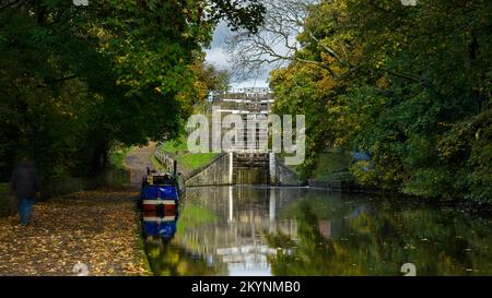 Péniche sur une voie navigable rurale ensoleillée, personne marchant sur le sentier, couleur d'automne - 5 écluses de hauteur, canal de Leeds Liverpool, Bingley, West Yorkshire, Angleterre Royaume-Uni. Banque D'Images