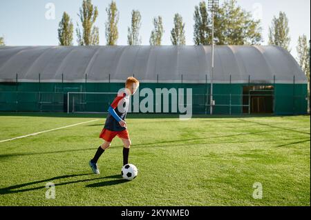 Un joueur de football de l'âge élémentaire s'entraîne à coups de pied sur le terrain de football Banque D'Images