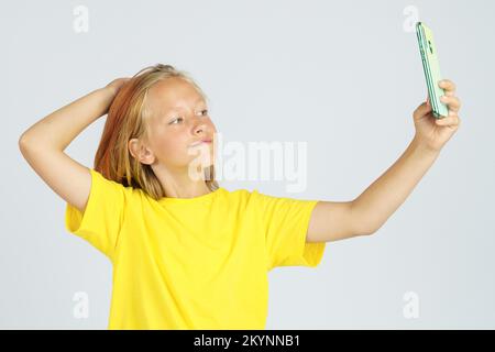 Une adolescente dans un T-shirt jaune prend un selfie sur un téléphone portable. Arrière-plan isolé. Concept d'éducation. Banque D'Images