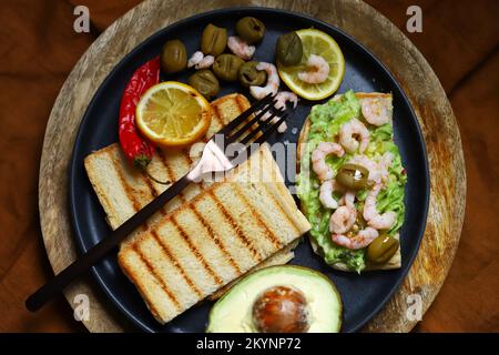 Toast au guacamole avec avocat, crevettes et olives. En-cas sain. Céto. Banque D'Images