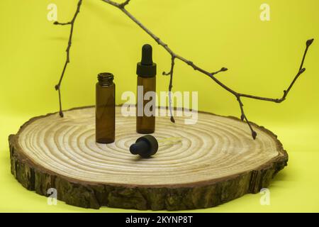 Maquette de flacons en verre brun avec couvercle compte-gouttes sur panneau en bois. Vider les flacons en verre avec pipette et branche d'arbre sur fond jaune. Concept de médicis Banque D'Images