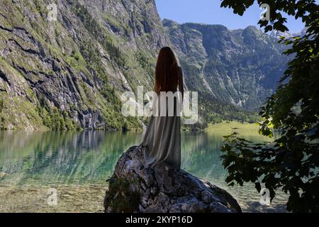 Une jeune femme se tient sur une pierre près d'un lac de montagne de couleur émeraude Banque D'Images