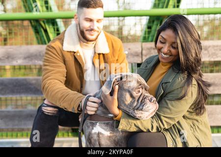 Heureux couple multiethnique marchant dans la ville et embrassant leur chien dans une journée d'hiver. Banque D'Images