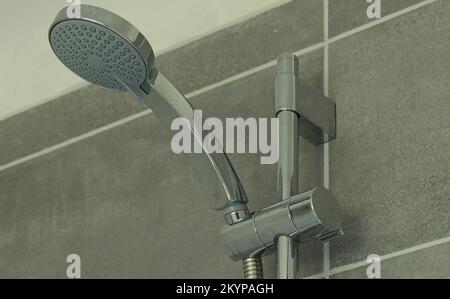 Vue rapprochée d'une pomme de douche et d'une barre de réglage chromée dans l'enceinte de la douche d'une salle de bains carrelée de gris Banque D'Images