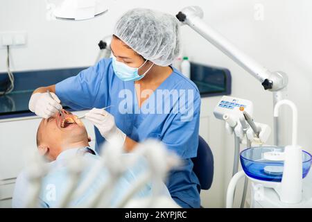 Le dentiste féminin examine la cavité buccale de la patiente.Soins dentaires en clinique dentaire Banque D'Images