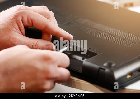 Les mains du réparateur en dévissant les vis du boîtier de l'ordinateur portable à l'aide d'un tournevis. Entretien et réparation informatiques. Démontage de l'ordinateur portable dans un atelier de réparation. Ele Banque D'Images