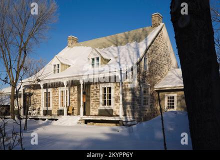 Vieux 1700s deux étages de style Canadiana maison en pierre de champ à travers les arbres en hiver. Banque D'Images