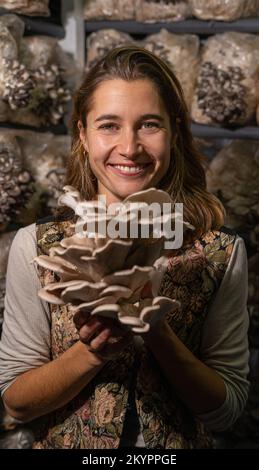 Jeune femme heureuse tenant des champignons d'huîtres contre la serre de champignons. Banque D'Images