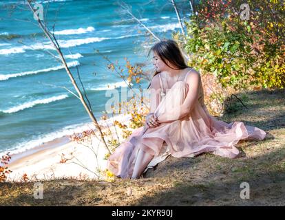 Jolie jeune femme dans une robe formelle, rêve une elle se détend sur un rebord haut au-dessus d'un lac turquoise Banque D'Images