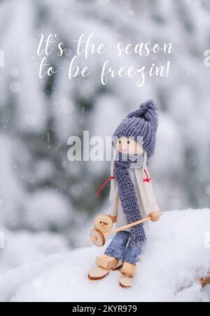 C'est la saison pour être Freezin inspiration plaisanterie citation phrase Angel gnome dans le foulard et chapeau tricoté ski sur la branche de sapin enneigé jouet Elf sur les skis dans le paysage neigeux Nouvelle année et carte de vœux Joyeux Noël. Station de vacances d'hiver verticale Banque D'Images