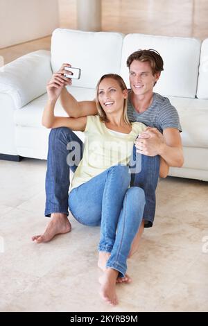 Immortalisez un moment intime. Un jeune couple prend des photos avec son téléphone portable dans son salon. Banque D'Images