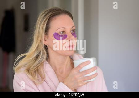 Vue latérale d'une jolie femme d'âge moyen dans son peignoir rose avec des yeux portant une tasse de café Banque D'Images