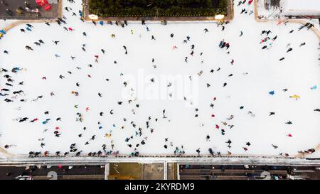 Vue de dessus des personnes qui patinent sur la grande patinoire en plein air le jour de l'hiver. Vol avec vue aérienne sur la foule de personnes qui patinent sur la glace à la patinoire. Sports d'hiver. Fond de patinage. Patinoire municipale. Banque D'Images