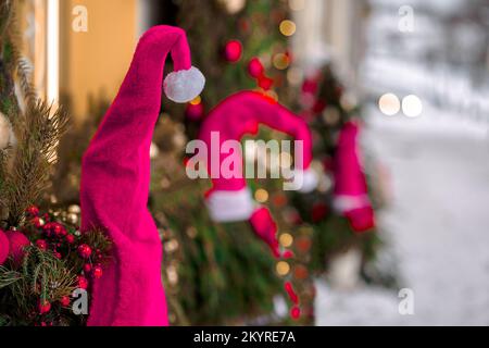 Tonalité en Viva Magenta. Arrière-plan abstrait de Noël d'hiver avec chapeaux de père noël rouges, branches de sapin de neige et lumières. Atmosphère douce et agréable dans des couleurs pastel. Design créatif tendance en couleur 2023. Banque D'Images