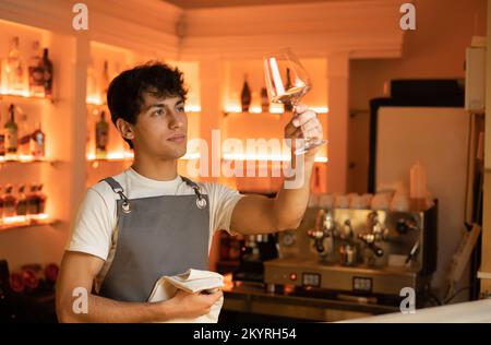 Barman polissage du verre à vin dans le café-bar, debout au comptoir avec des bouteilles sur le fond. Copier l'espace Banque D'Images