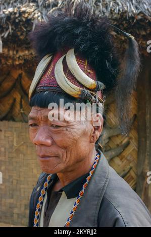 Mon, Nagaland, Inde - 02 28 2013 : Portrait d'un homme de tribu Naga Konyak avec un style de cheveux typique portant un chapeau de canne rouge traditionnel avec des défenses de sanglier et de la fourrure Banque D'Images