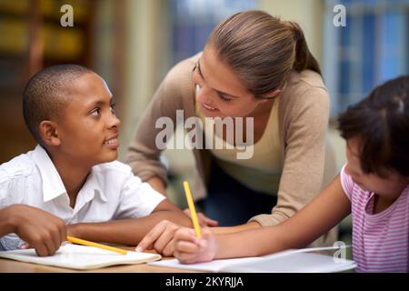 Elle enseigne de son cœur. une enseignante aidant ses élèves avec leur travail dans la salle de classe. Banque D'Images