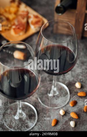 Deux verres de vin rouge sont sur la table. Prosciutto au fromage, vin rouge, baguette, noix. Vin rouge et en-cas méditerranéens traditionnels. Banque D'Images
