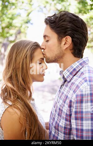 Un moment tendre ensemble. un beau jeune homme embrassant son front de copines tout en se tenant à l'extérieur dans un parc. Banque D'Images