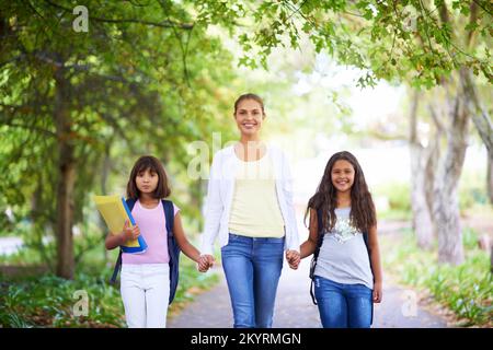 Les amener à l'école. Une enseignante marchant avec ses deux élèves à l'école. Banque D'Images