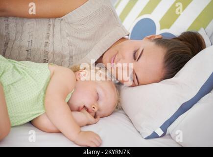 Shes toujours près de son bébé. Une jeune mère couchée à côté de son bébé endormi sur le lit. Banque D'Images