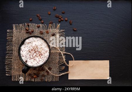 Tasse à café sur toile de jute rustique et carte en papier vierge. Vue de dessus avec espace de copie pour votre texte. fond noir, cappuccino. étiquette de prix Banque D'Images