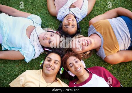 Nous avons collé par la musique. Angle élevé d'un groupe d'amis allongé sur le dos sur l'herbe dans un parc. Banque D'Images